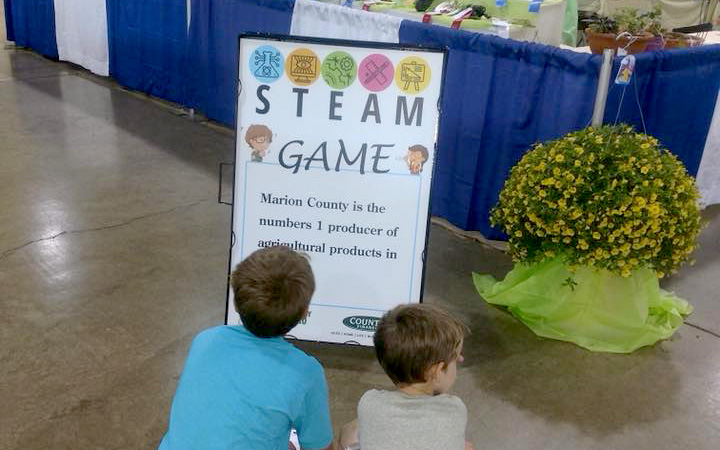 kids kneeling to look at a sandwich board sign talking about the STEAM quest at Marion County Fair